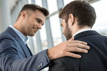 企業のオフィスで、同僚の肩に手を置き、安心させ、サポートと励ましを与えるプロフェッショナルなビジネスマン。