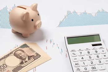 日本円の新紙幣の一万円札と株価チャートと貯金箱と電卓で株式投資のイメージ