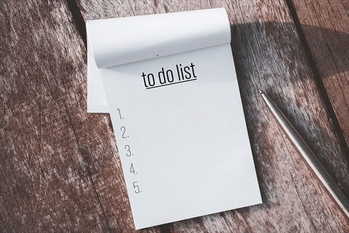 Notebook and pen with to do list words on wooden table background.