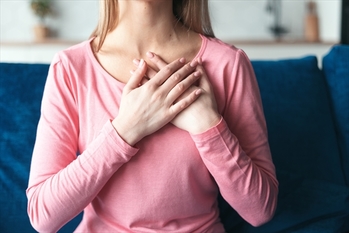 Woman hold hand folded close to heart in peaceful sign