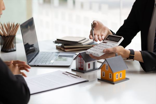 Businessman, real estate agent holding a calculator, presenting a price quote to a client for a house