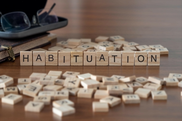 habituation word or concept represented by wooden letter tiles on a wooden table with glasses and a book