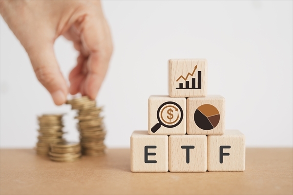 wooden cube with ETF text , Exchange Traded Fund and blurred hand with stack of coins.