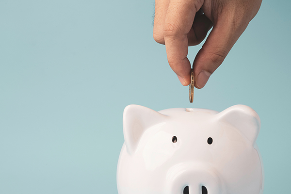 Hand putting coin to white piggy bank saving on blue background and copy space