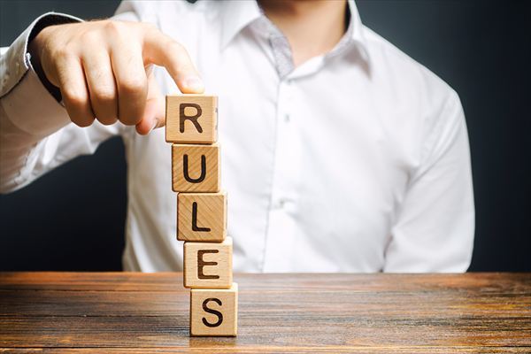 「ルール」と書かれたブロックの塔を、倒れないように男性が支えている