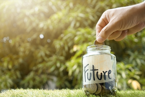 Hand putting coin in glass jar with coins inside For now and future money